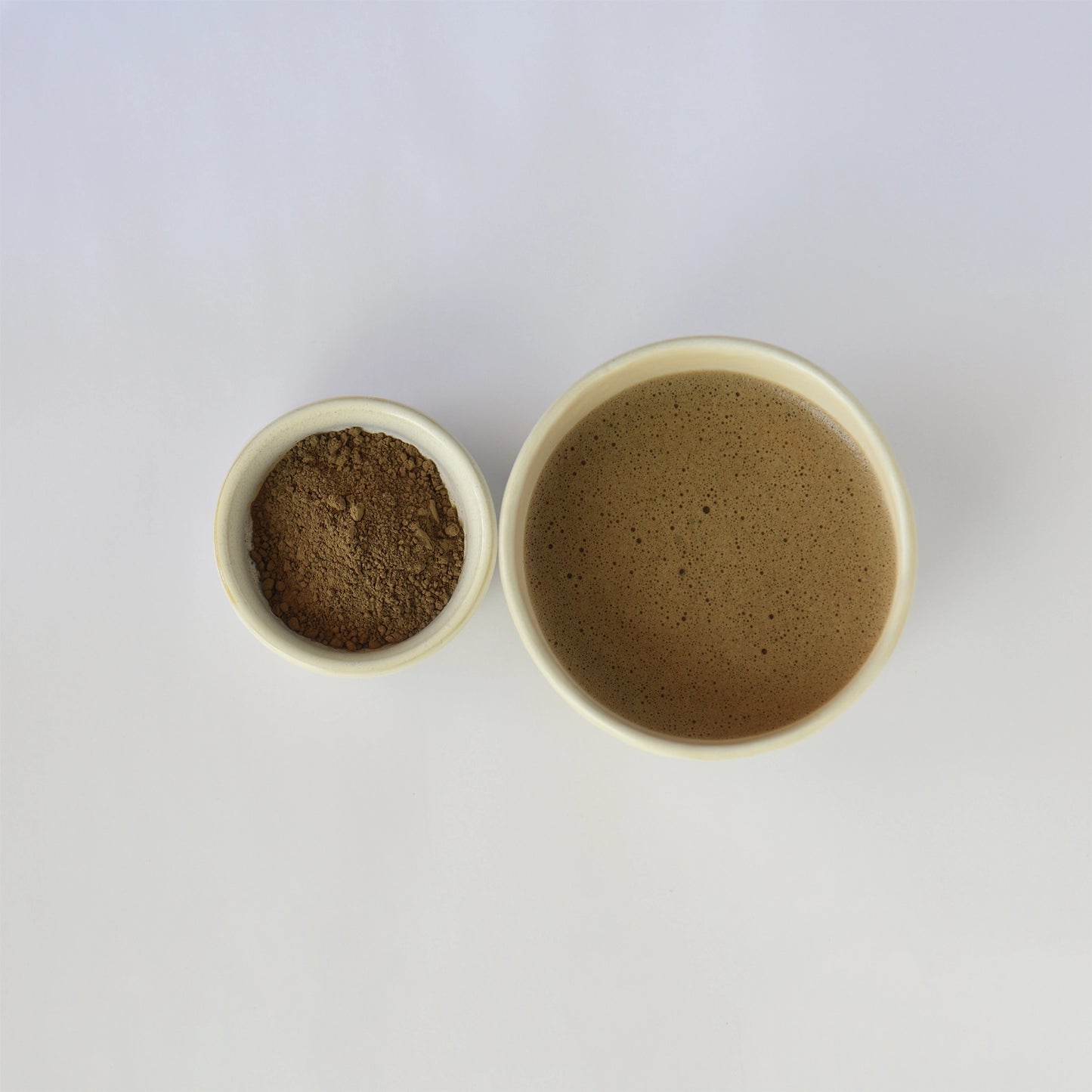 Two small ceramic bowls, one filled with a light roast hojicha powder and the other light roast hojicha on a white background