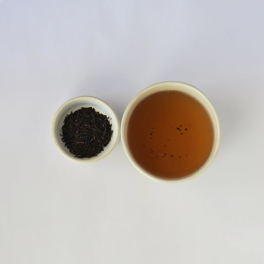 Tea leaves in a small bowl next to a cup of brewed tea on a white background