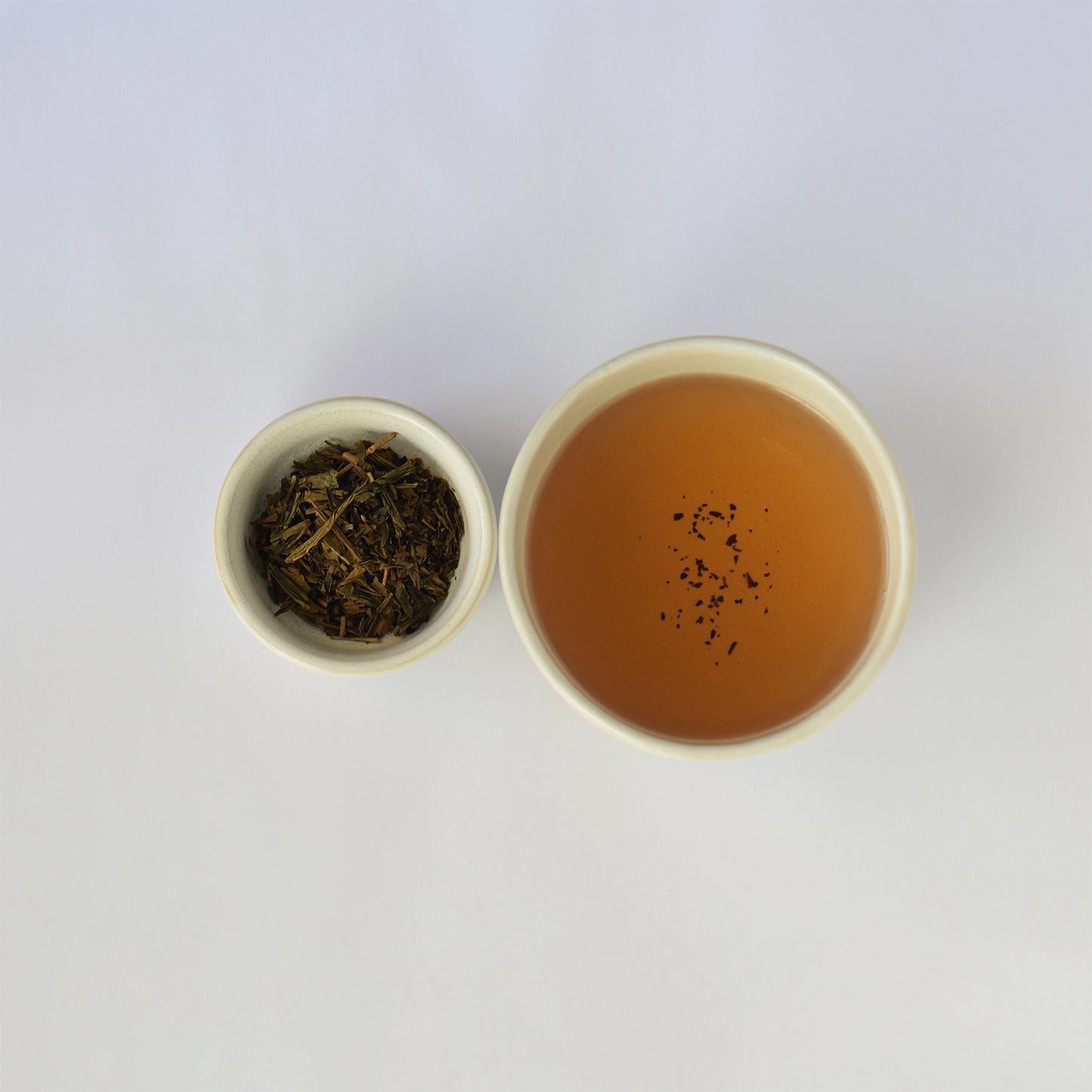 Tea leaves in a small container next to a cup of brewed tea on a white background