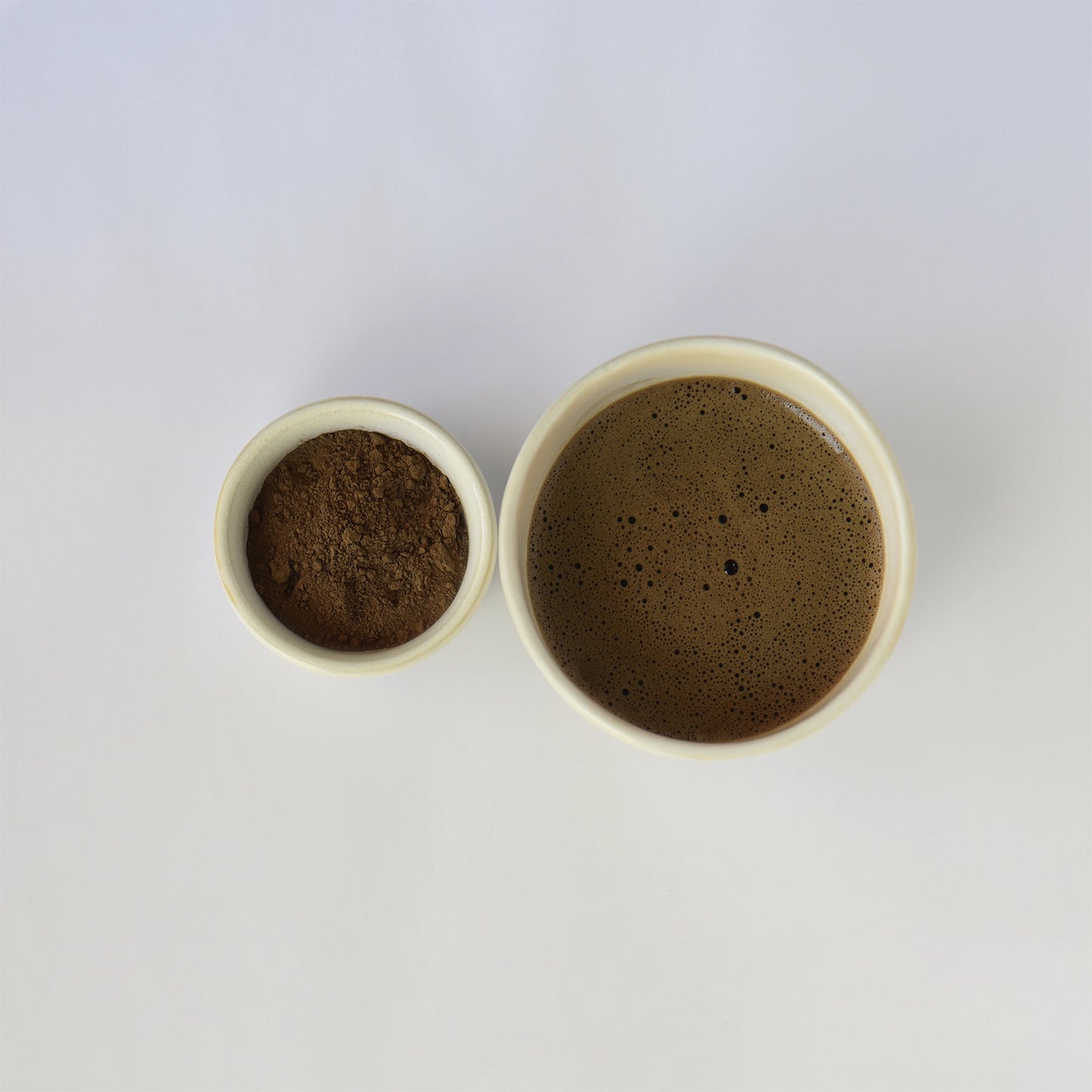 Two small ceramic bowls, one filled with a dark roast hojicha powder and the other dark roast hojicha on a white background