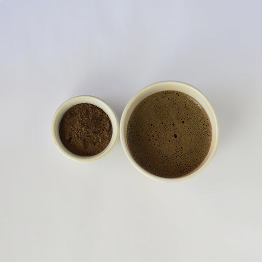 Two small ceramic bowls, one filled with a dark roast hojicha powder and the other dark roast hojicha on a white background