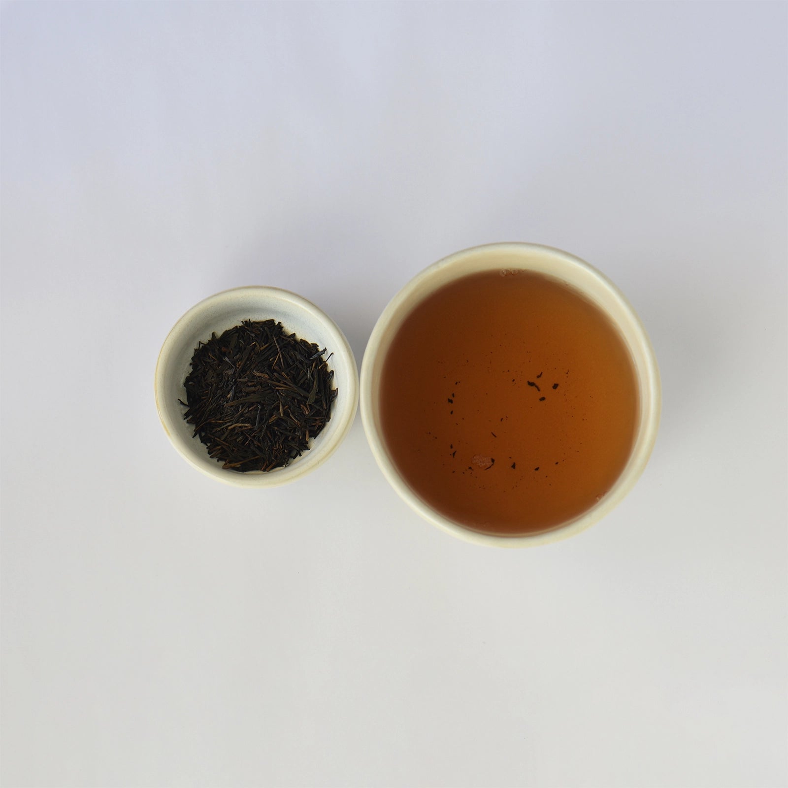 Tea leaves in a small bowl next to a cup of brewed tea on a white background