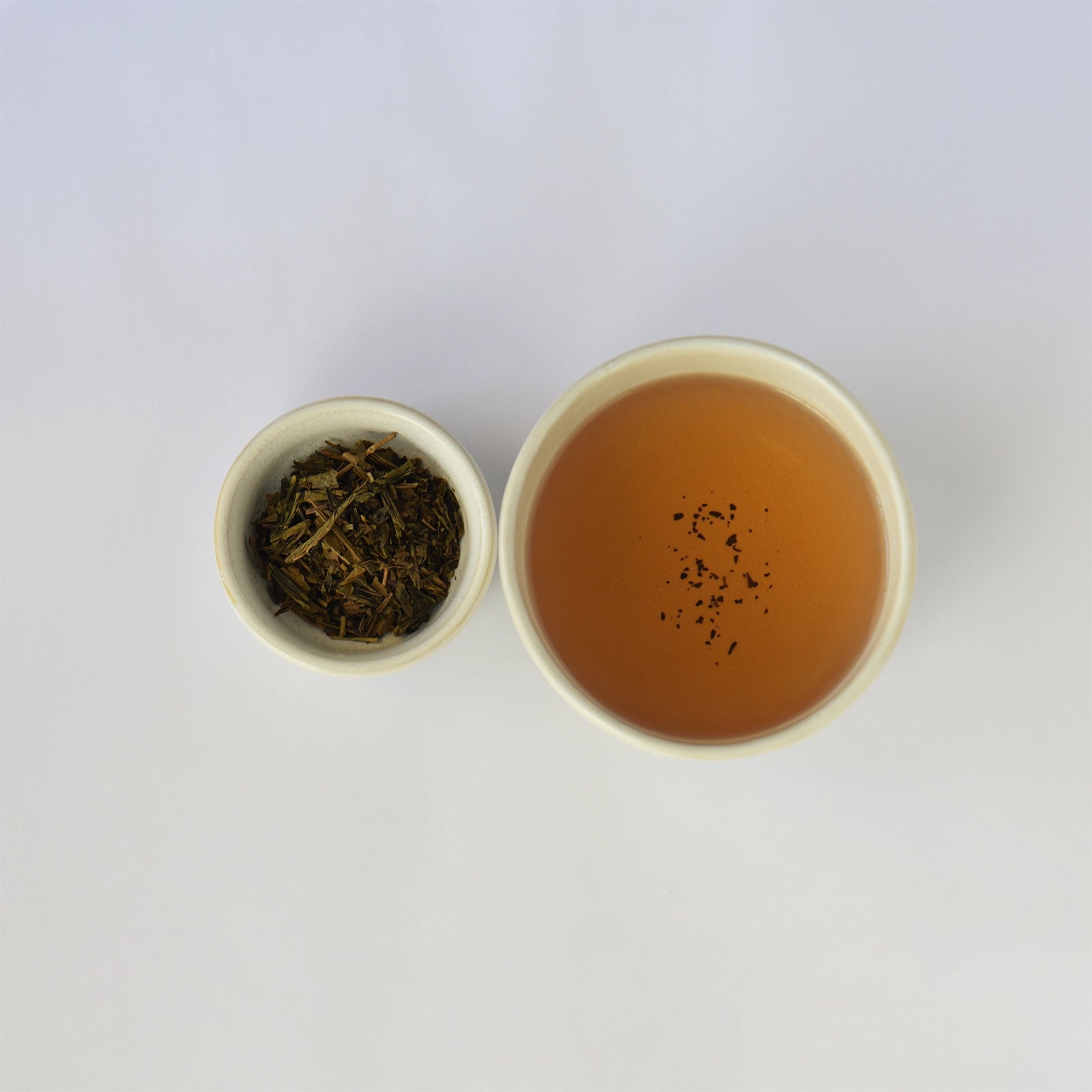 Tea leaves in a small container next to a cup of brewed tea on a white background