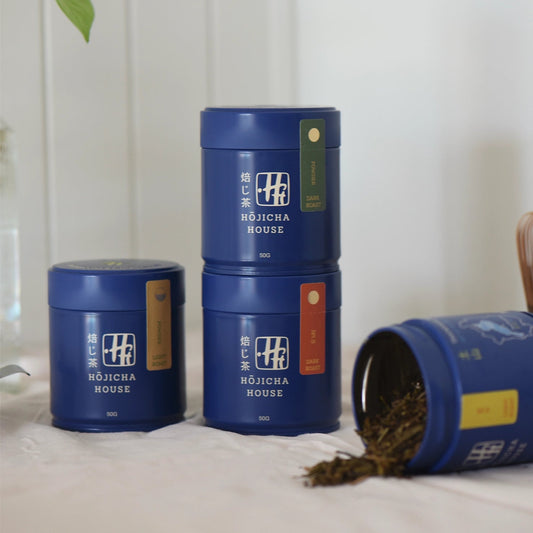 Three blue containers labeled 'Hojicha House' on a white surface with a plant in the corner.